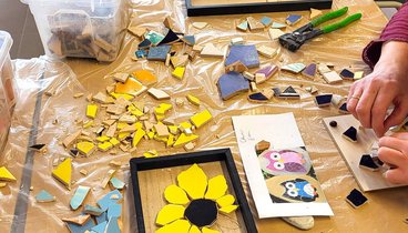 Personen gestalten bunte Mosaike aus Keramik und Glas mit verschiedenen Werkzeugen